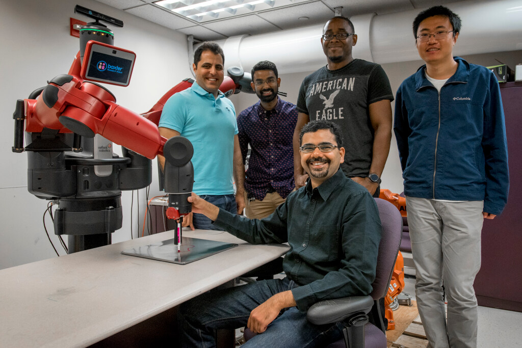 faculty and graduate students in front of a robotic arm